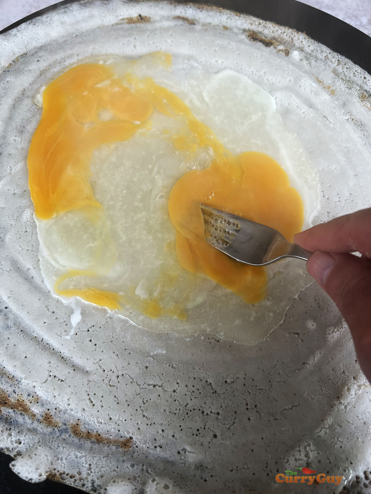 Breaking and then spreading the eggs over the dosa surface.