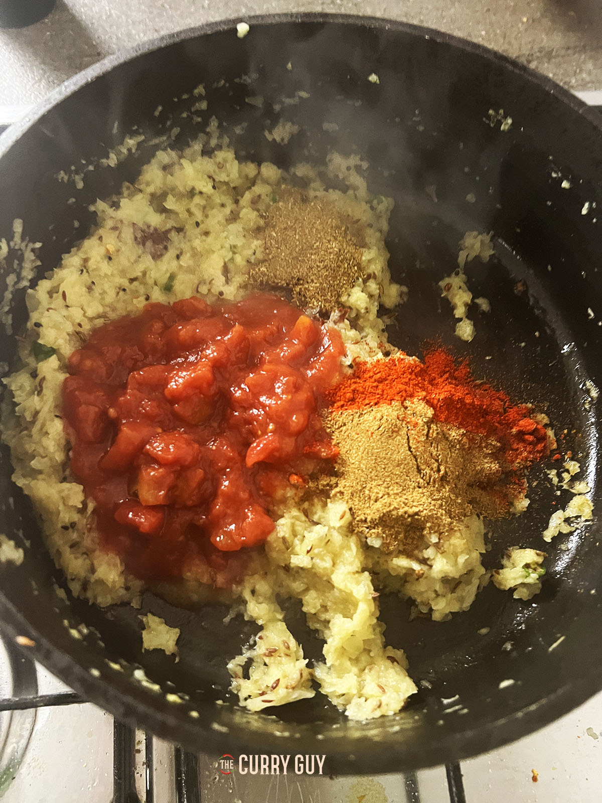 Adding chopped tomatoes and ground spices to the pan.