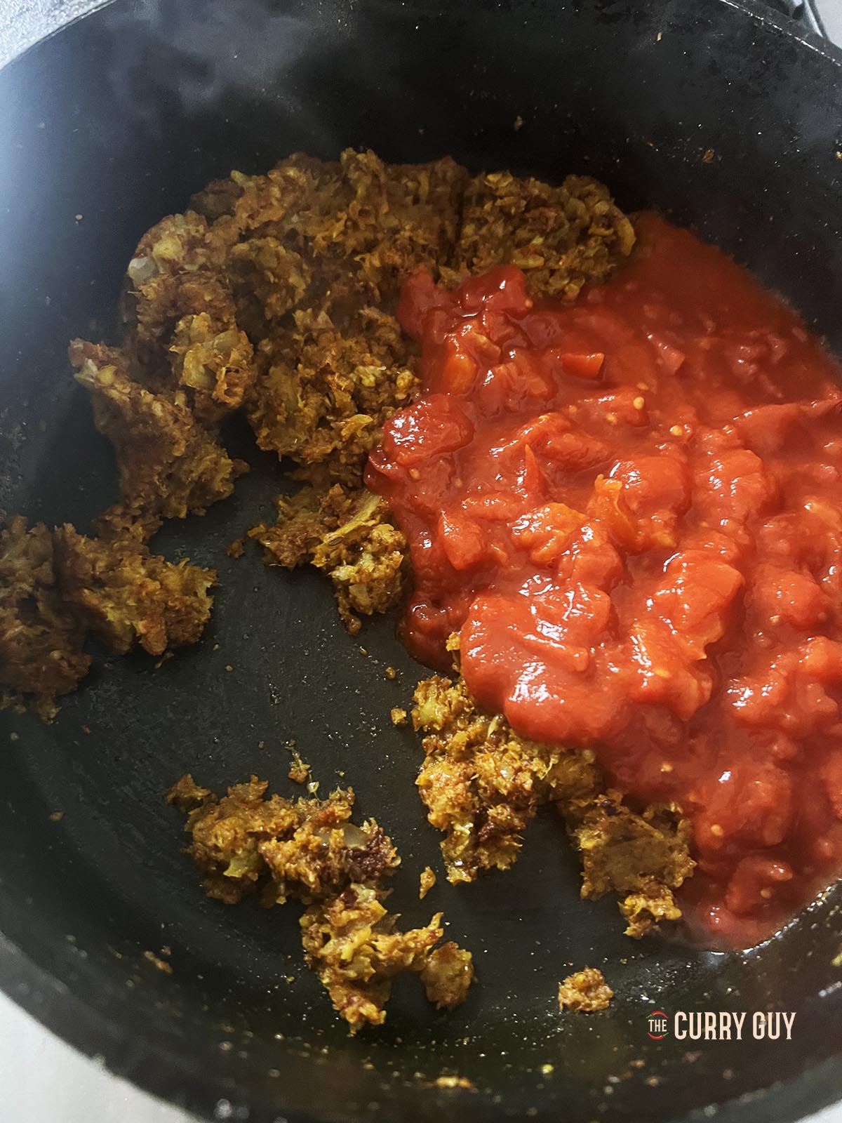 Stirring the spices into the onions and adding chopped tomatoes to the pan.