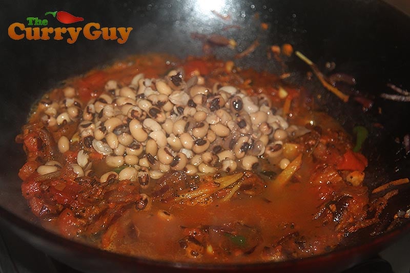 Adding turmeric, chilli powder and the black eyed peas to the pan.