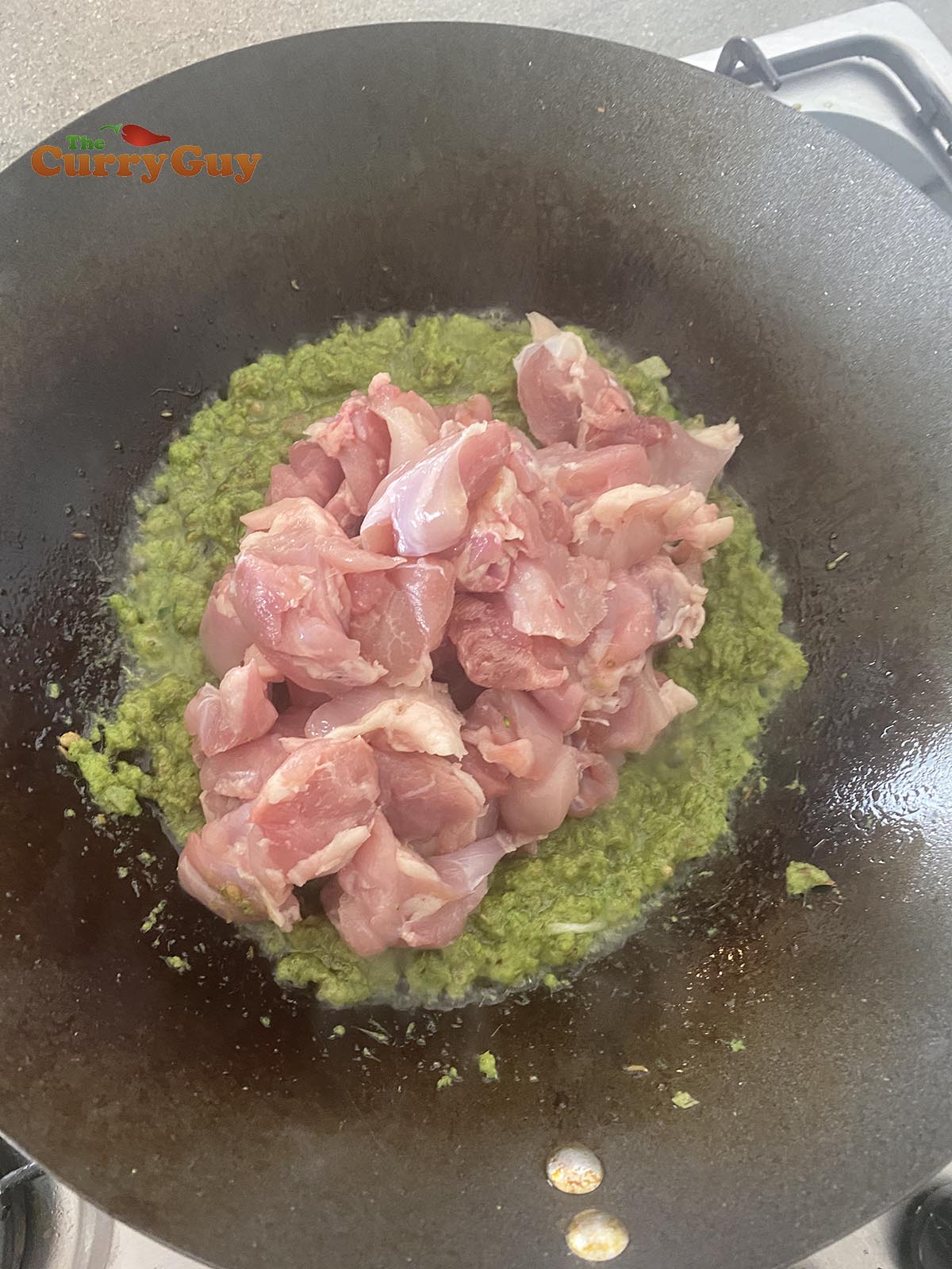 adding chicken to the green curry paste pan