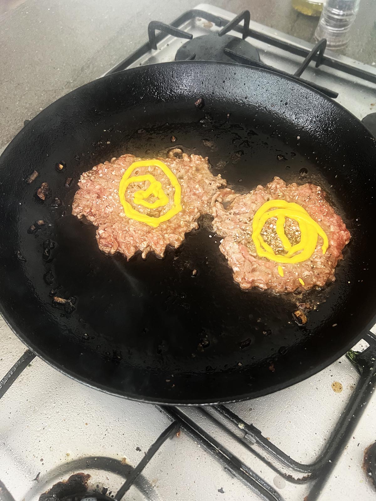 Seasoning and adding mustard to the burger patties in the pan.