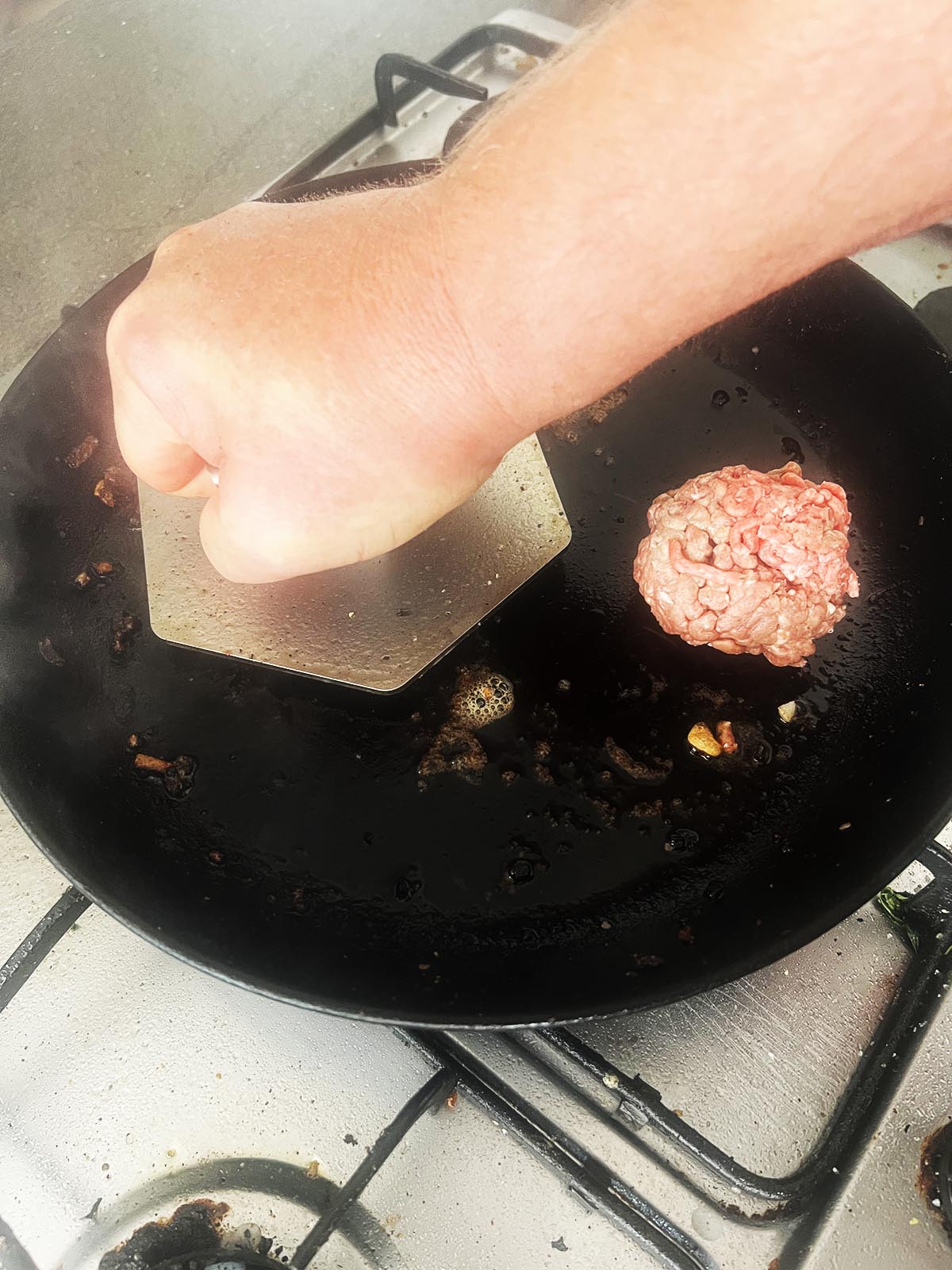 Pressing the burgers down flat with a burger press.