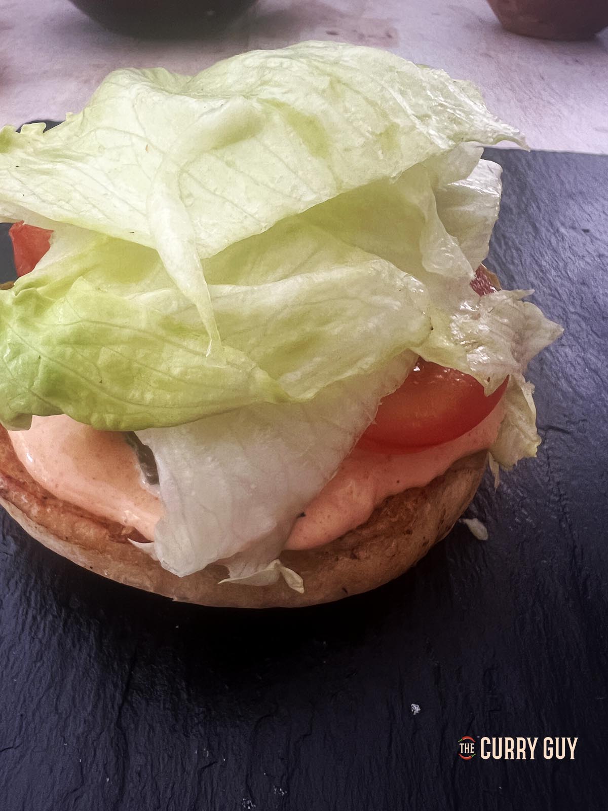Adding lettuce to the bottom bun before adding the cheesy burger patties and top bun.