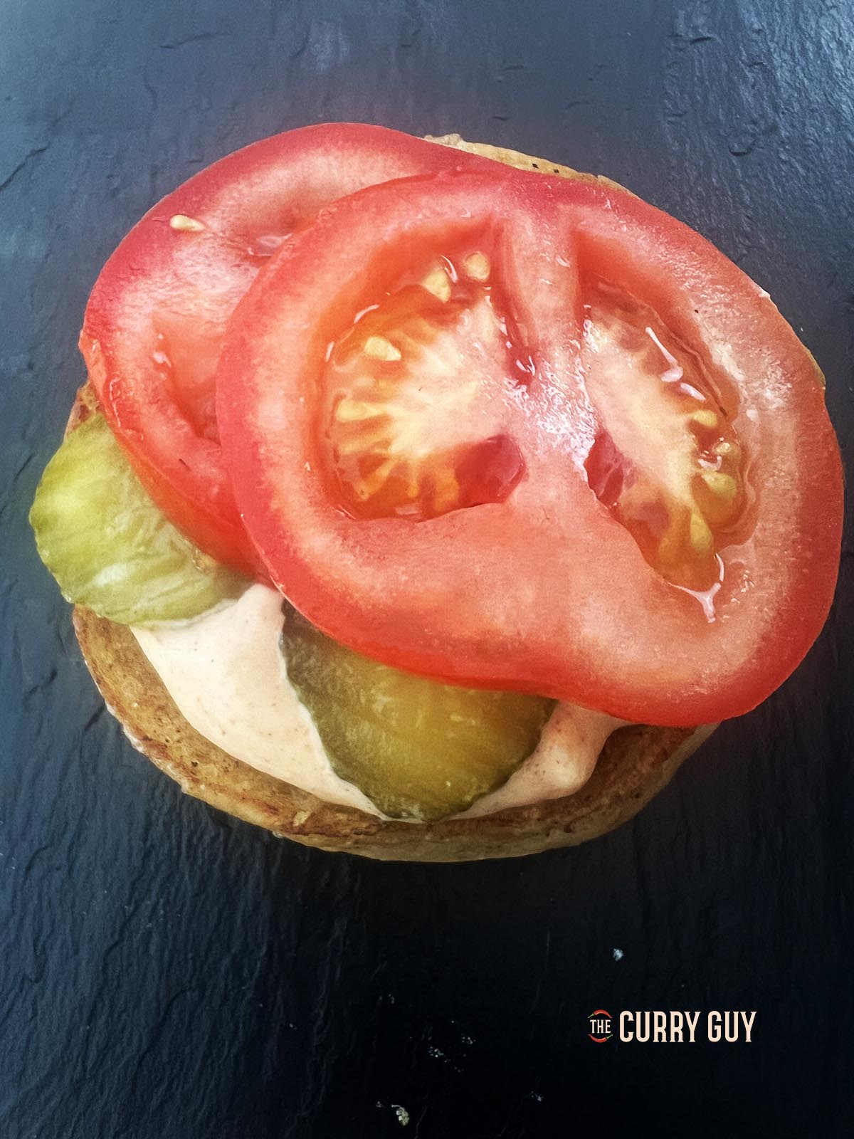 Adding burger sauce, pickle slices and tomato to the bottom bun.