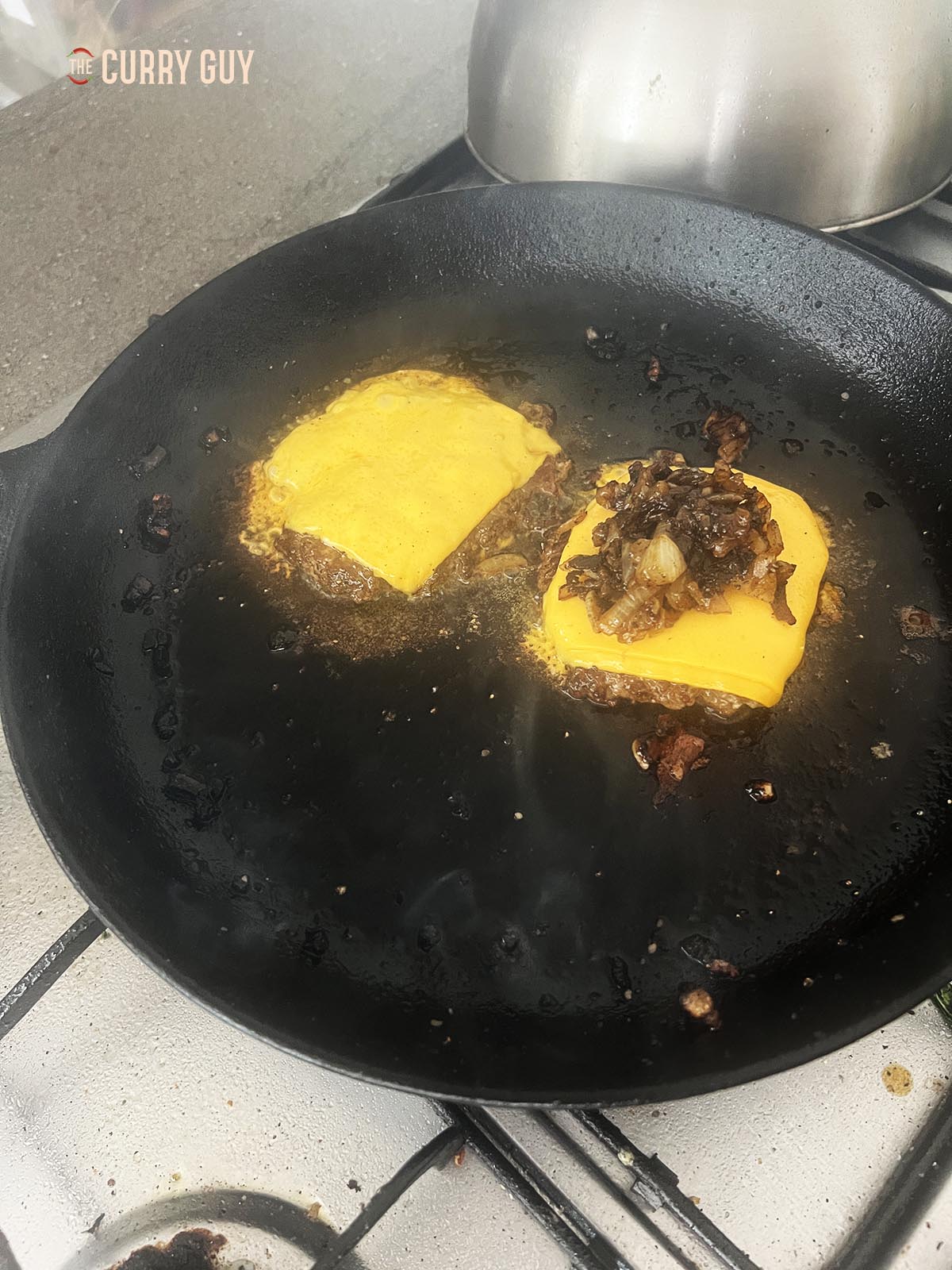 Topping the melted cheese on one of the burger patties with fried onions.