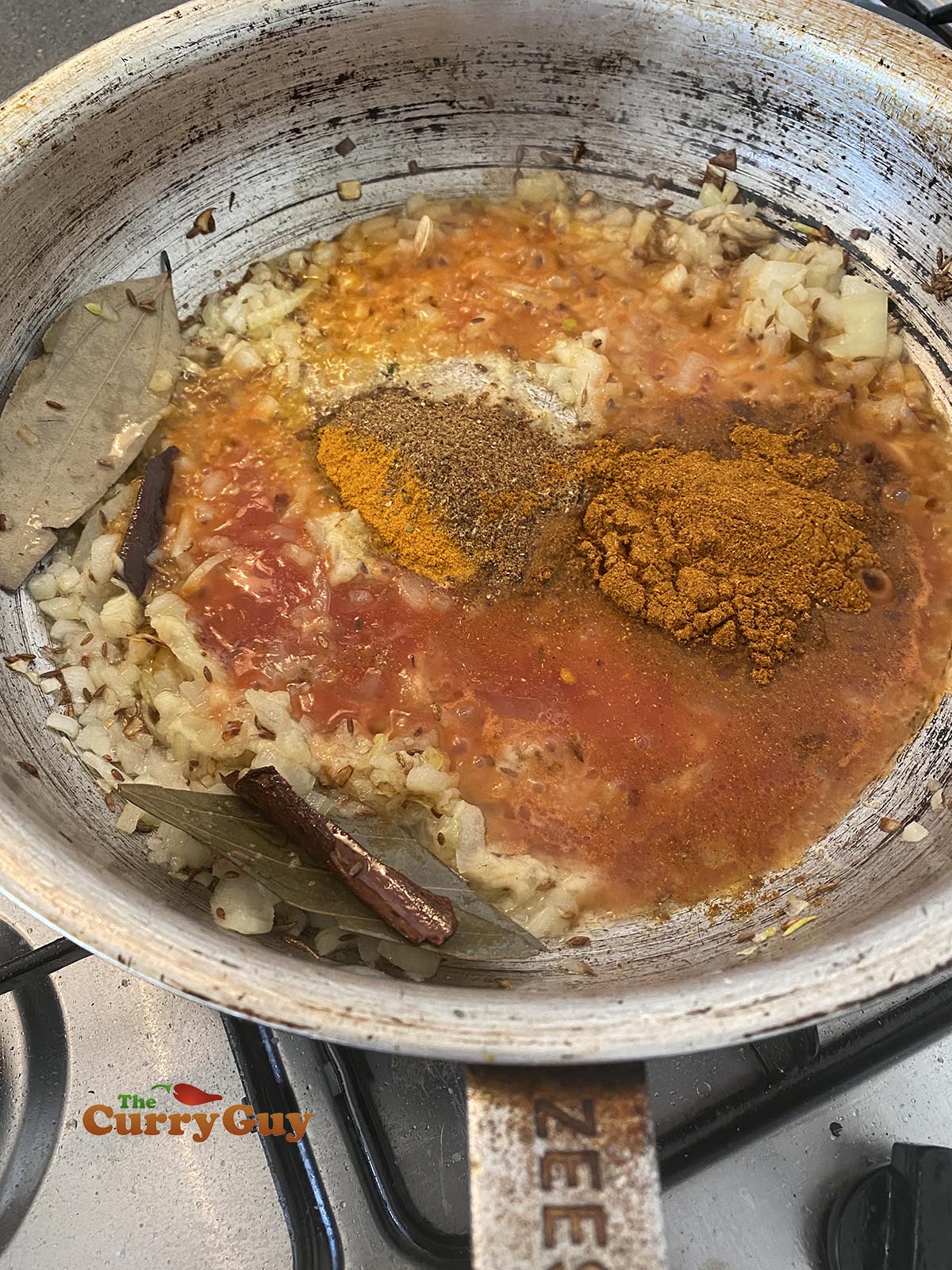 adding tomato puree and ground spices to the pan