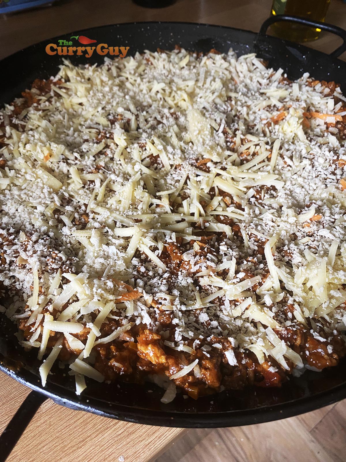 Adding the cheeses and bread crumbs to the top before placing the curry doria in the oven to finish cooking.