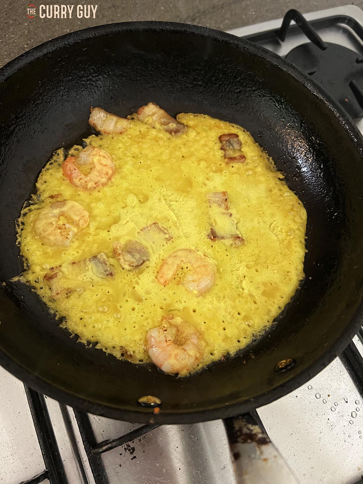 Adding batter to the pan with the shrimp and pork. 