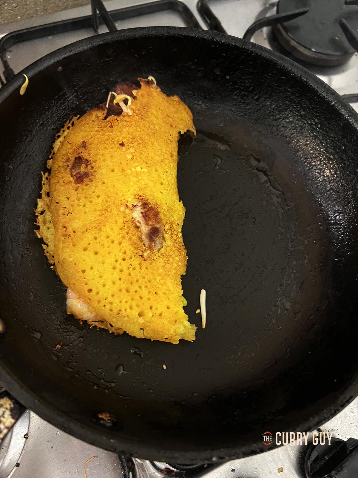 A cooked banh xeo folded over in a pan. 