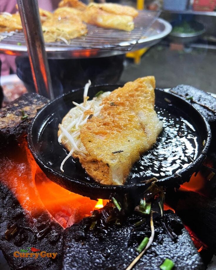 Banh xeo being cooked in a cast iron pan.