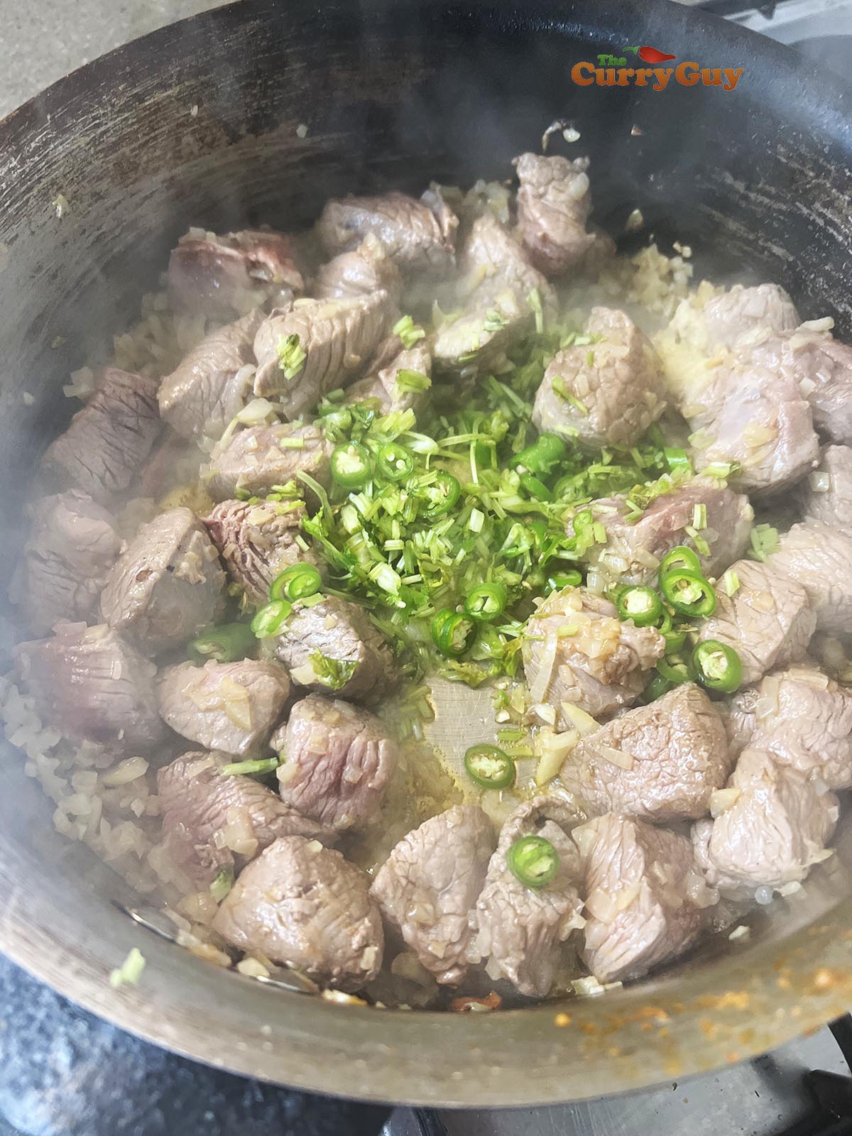 Adding coriander and chillies to the browned meat.
