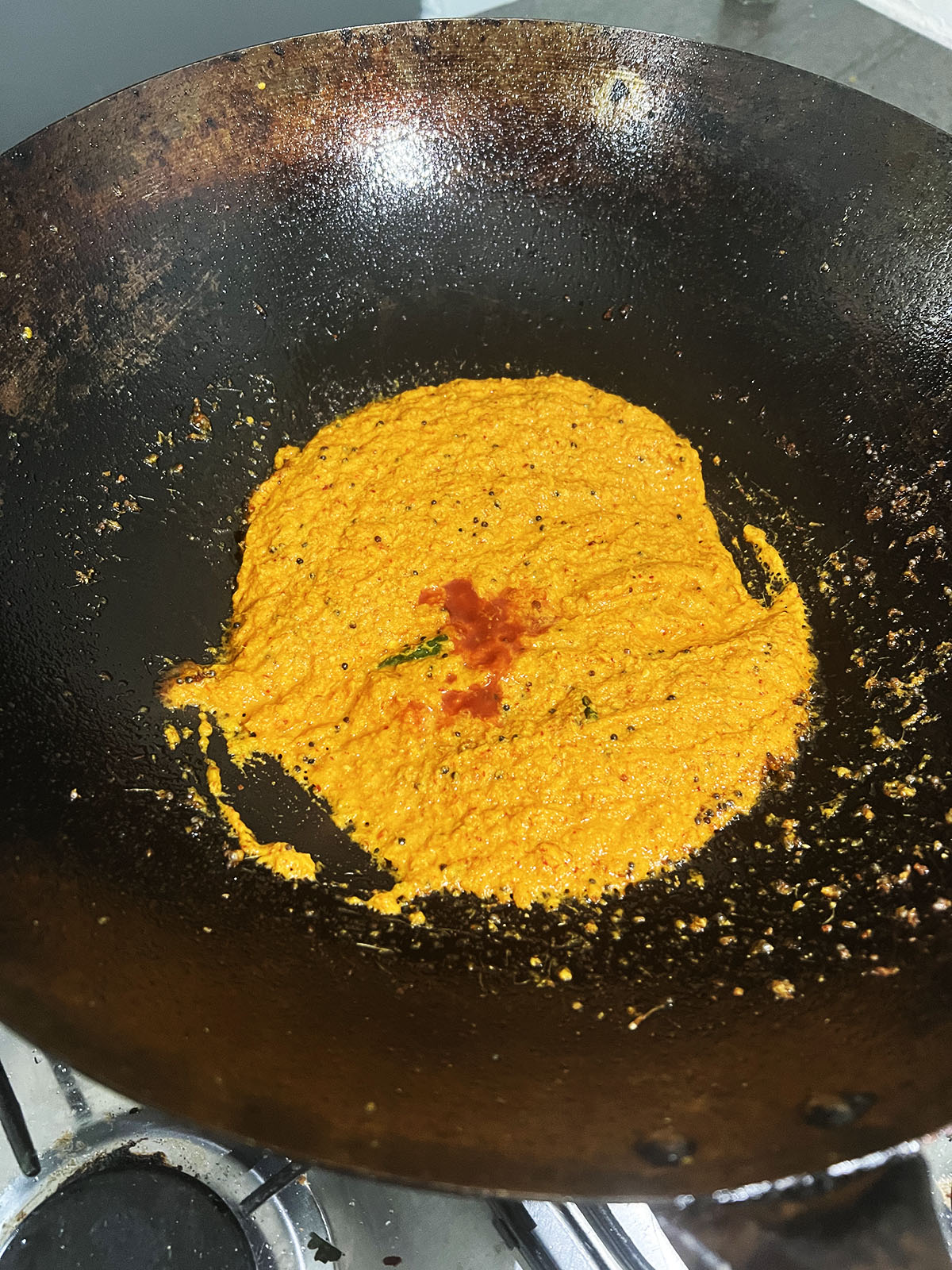 Adding tomato puree to the wok and stirring it into the curry paste