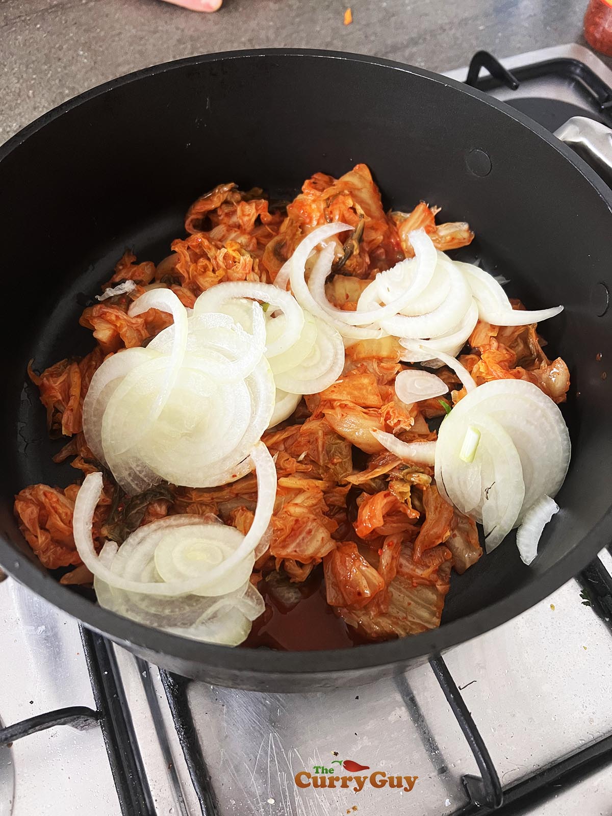 Adding kimchi brine, kimchi and onions to the pot
