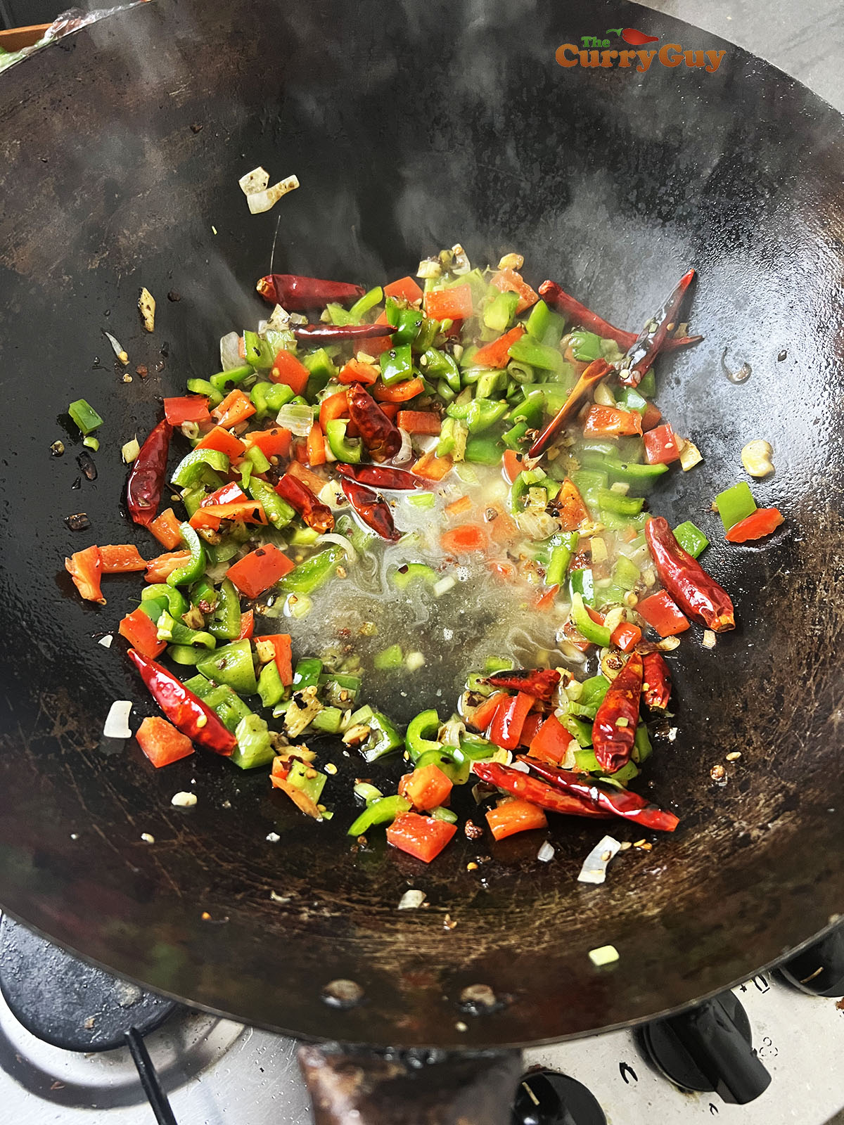 Adding chicken stock to the wok and bringing to a simmer.