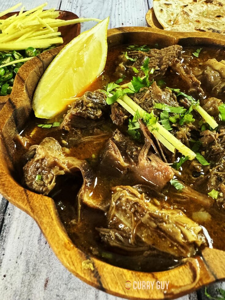 Beef nihari at the table in a serving dish and garnished with ginger, coriander and chillies.