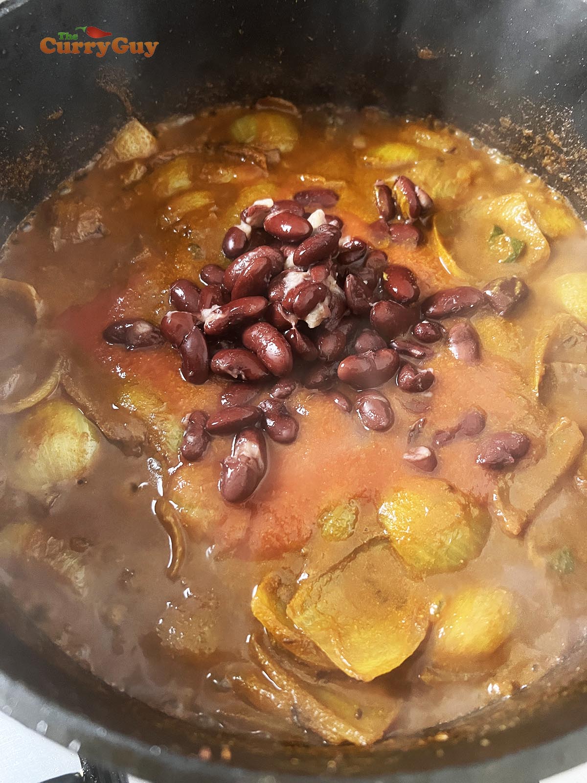 Adding tomato puree and kidney beans to the rajma masala