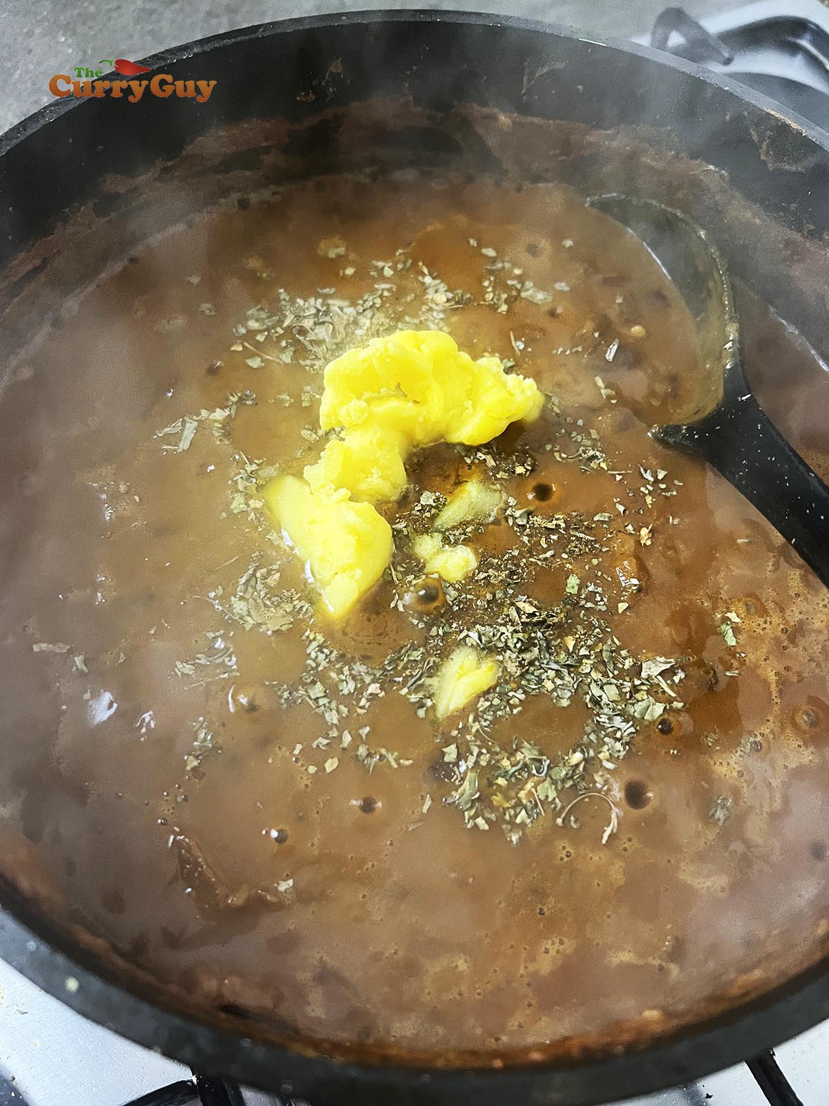 Adding ghee and kasoori methi (dried fenugreek leaves) to the curry.