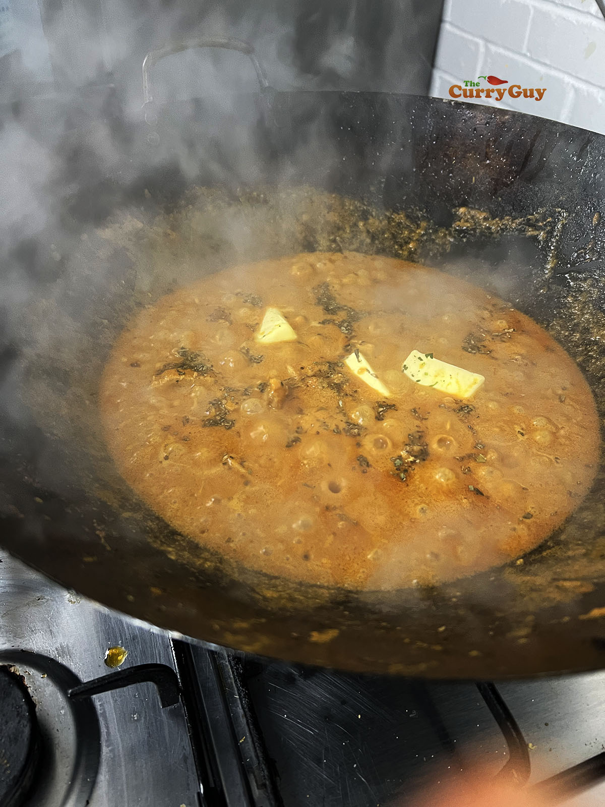 Adding butter and kasoori methi (dried fenugreek leaves).