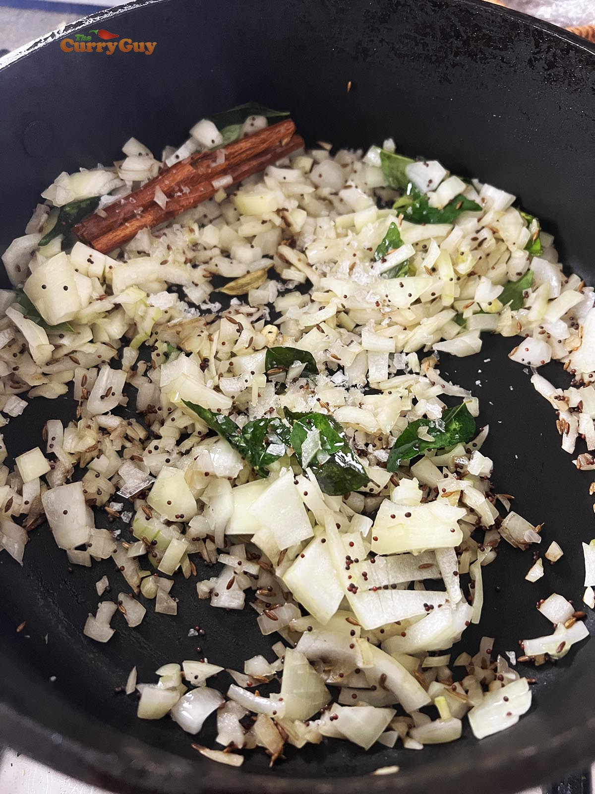 Adding chopped onions to the spices and oil.