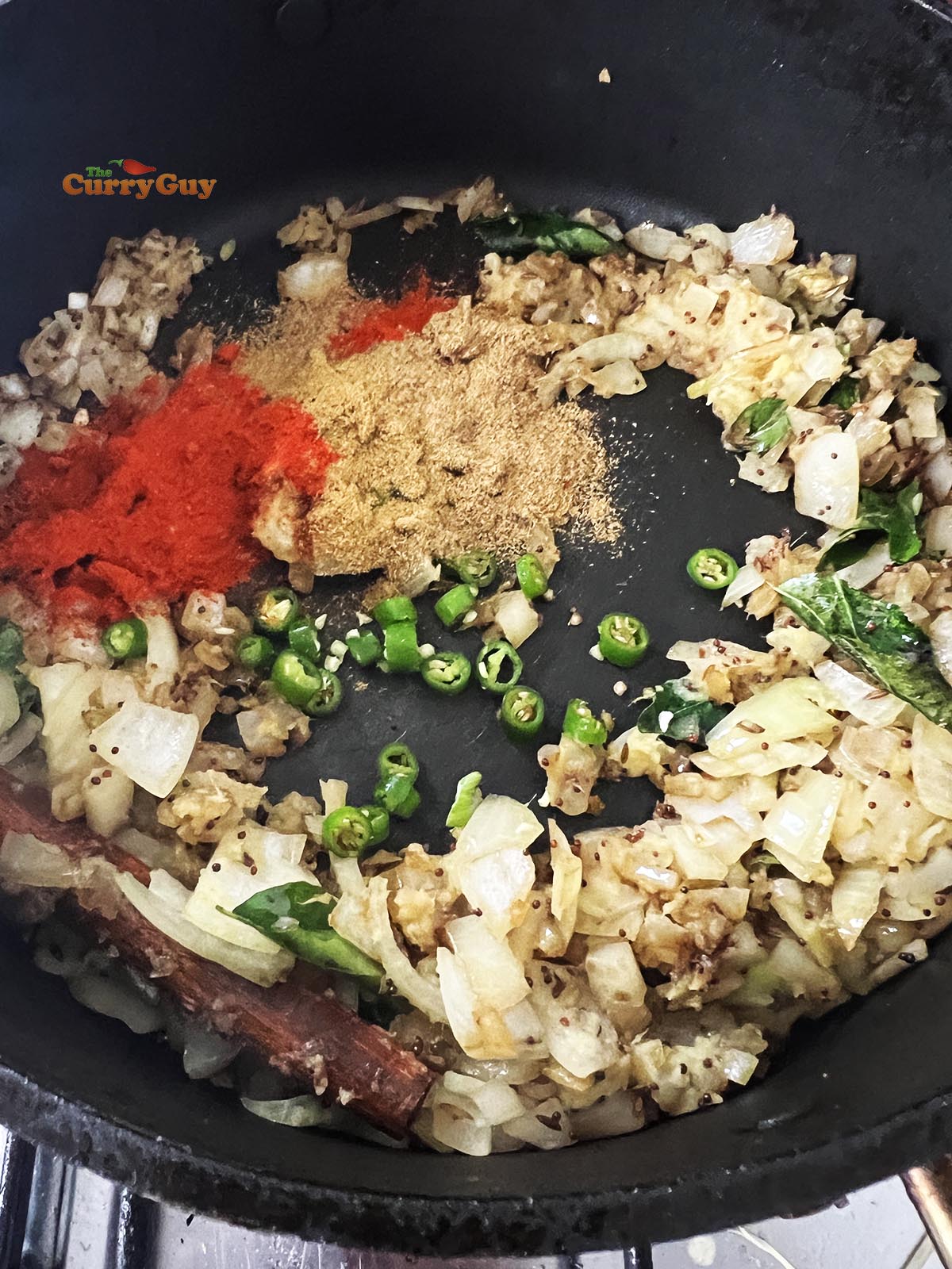 Adding the ground spices and chillies to the curry.