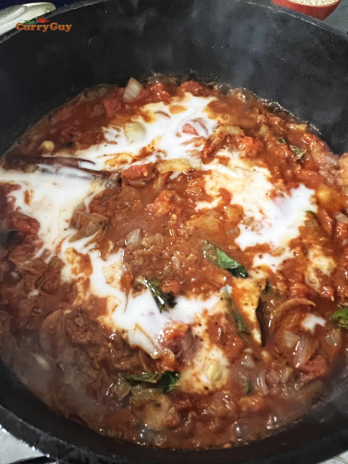 Adding coconut milk to the simmering sauce.