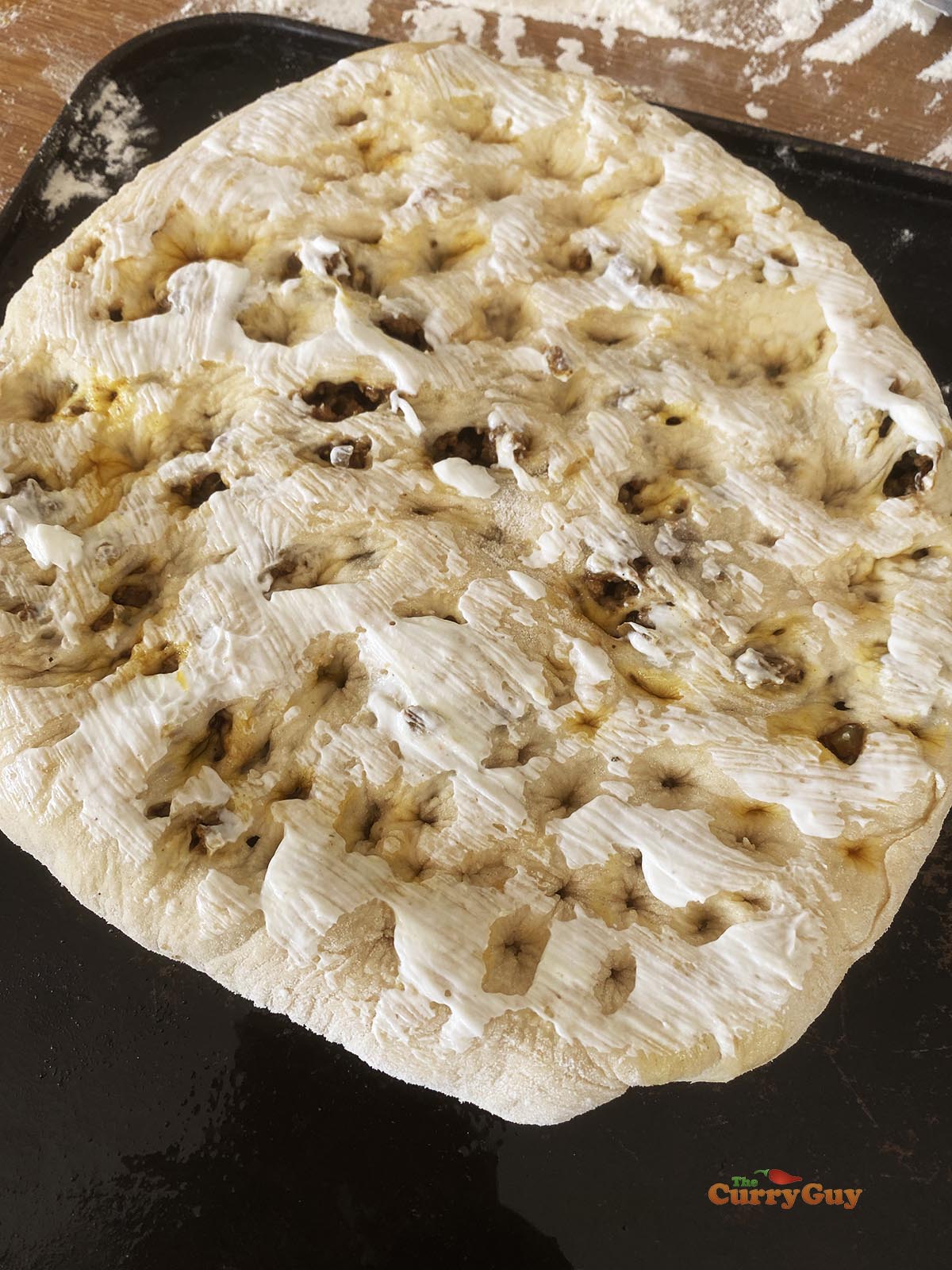 Spreading yoghurt over the surface of the naan.
