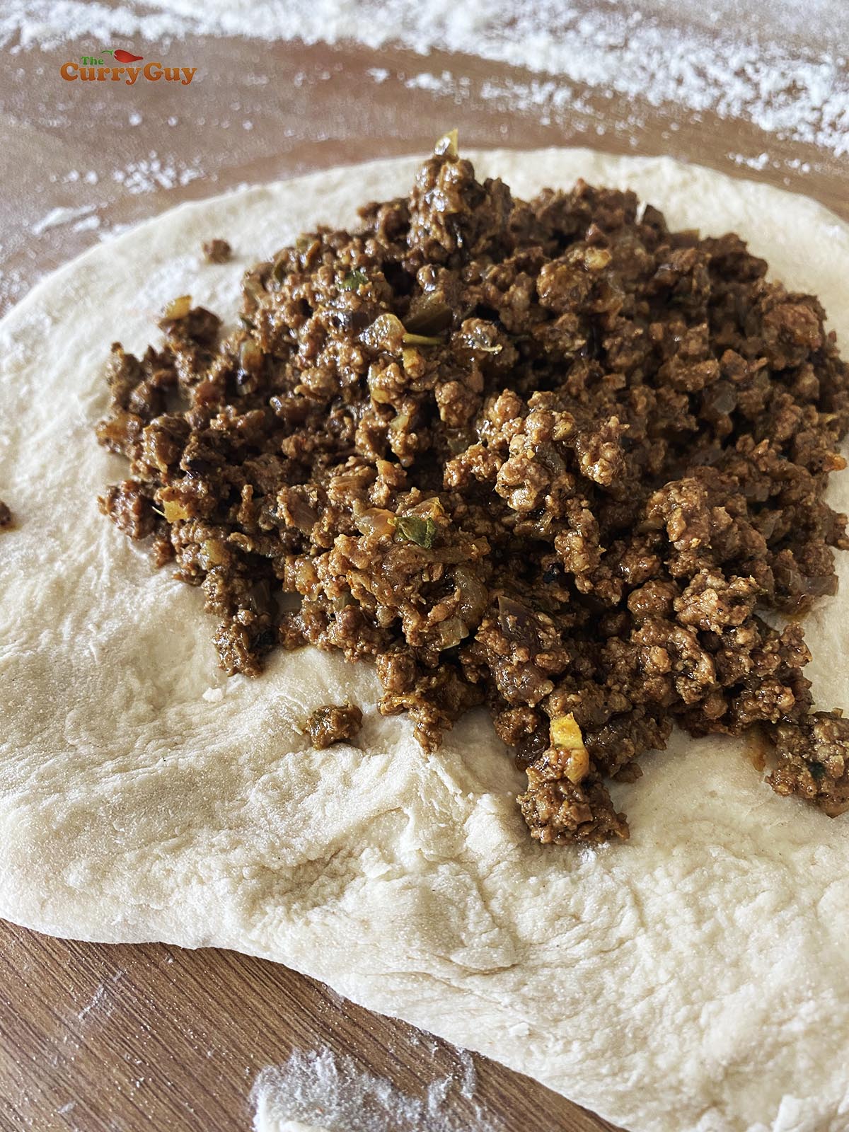 Topping a rolled out piece of dough with the keema curry.
