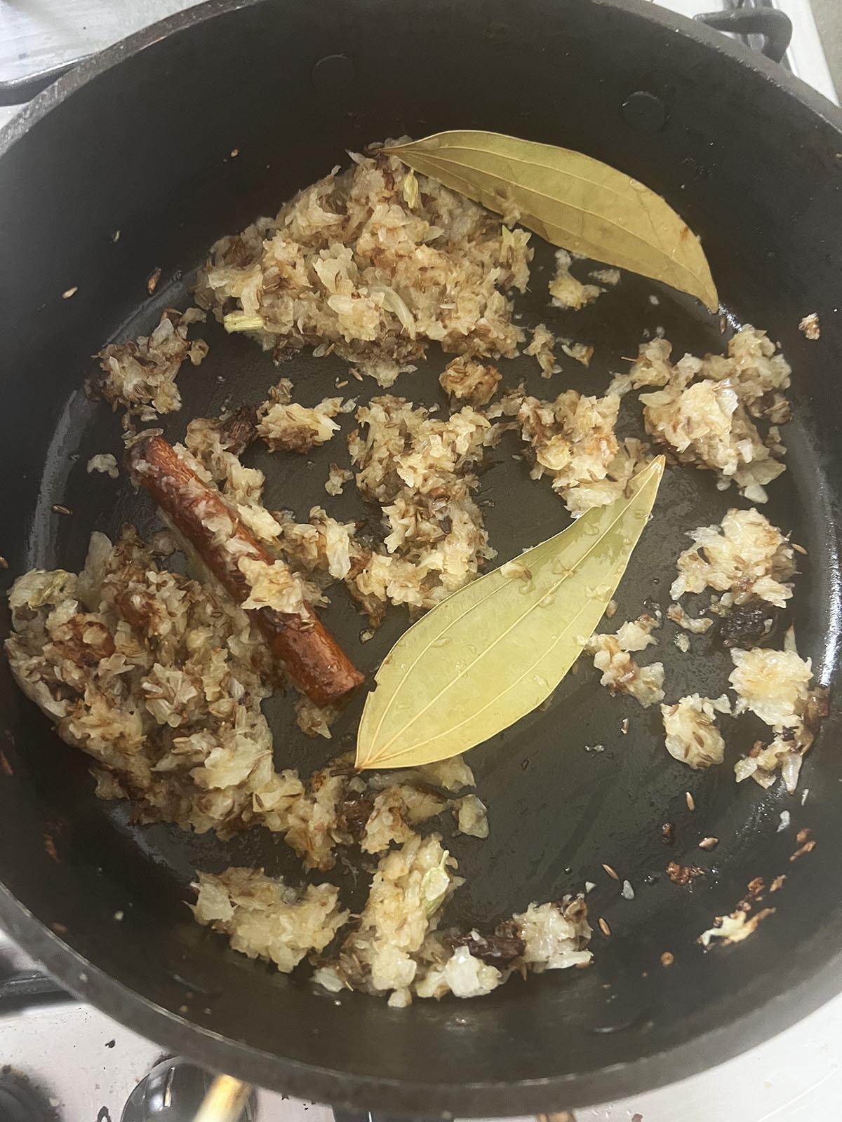 Frying whole spices and chopped onions in a pan.