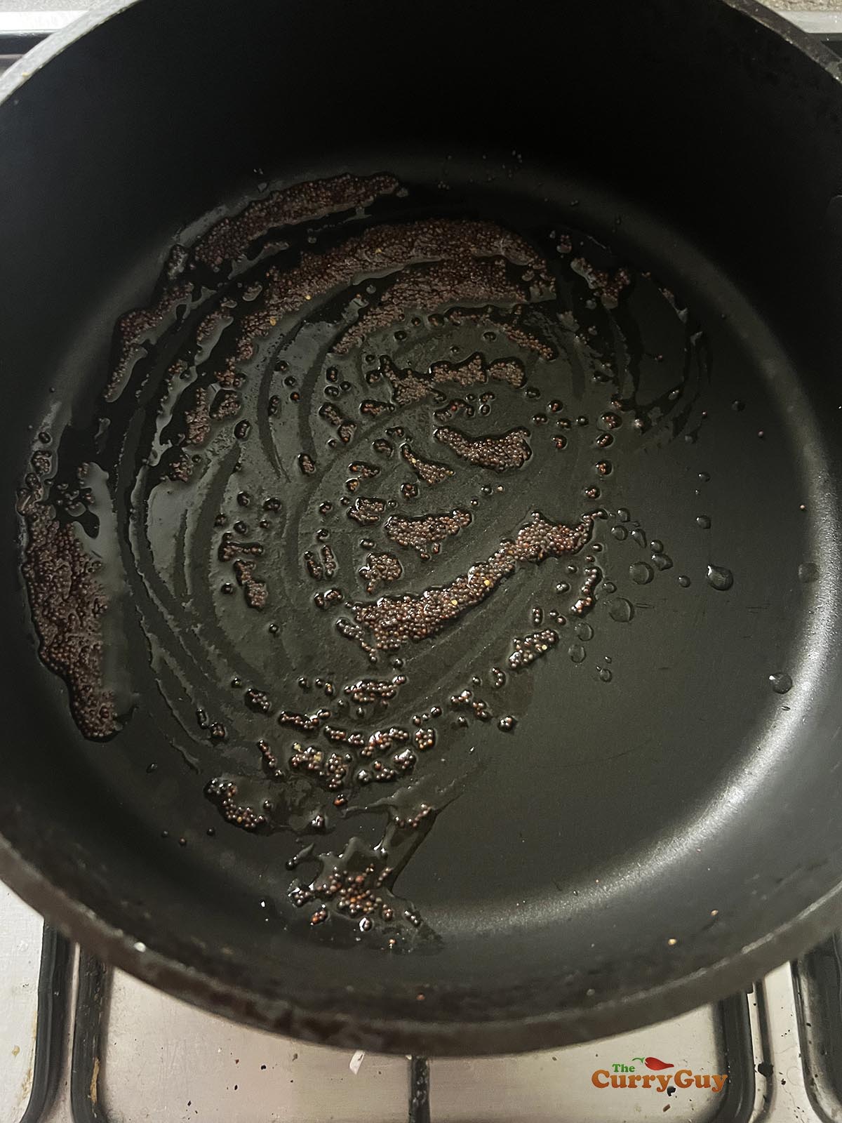 Infusing mustard seeds into hot oil in a pan.