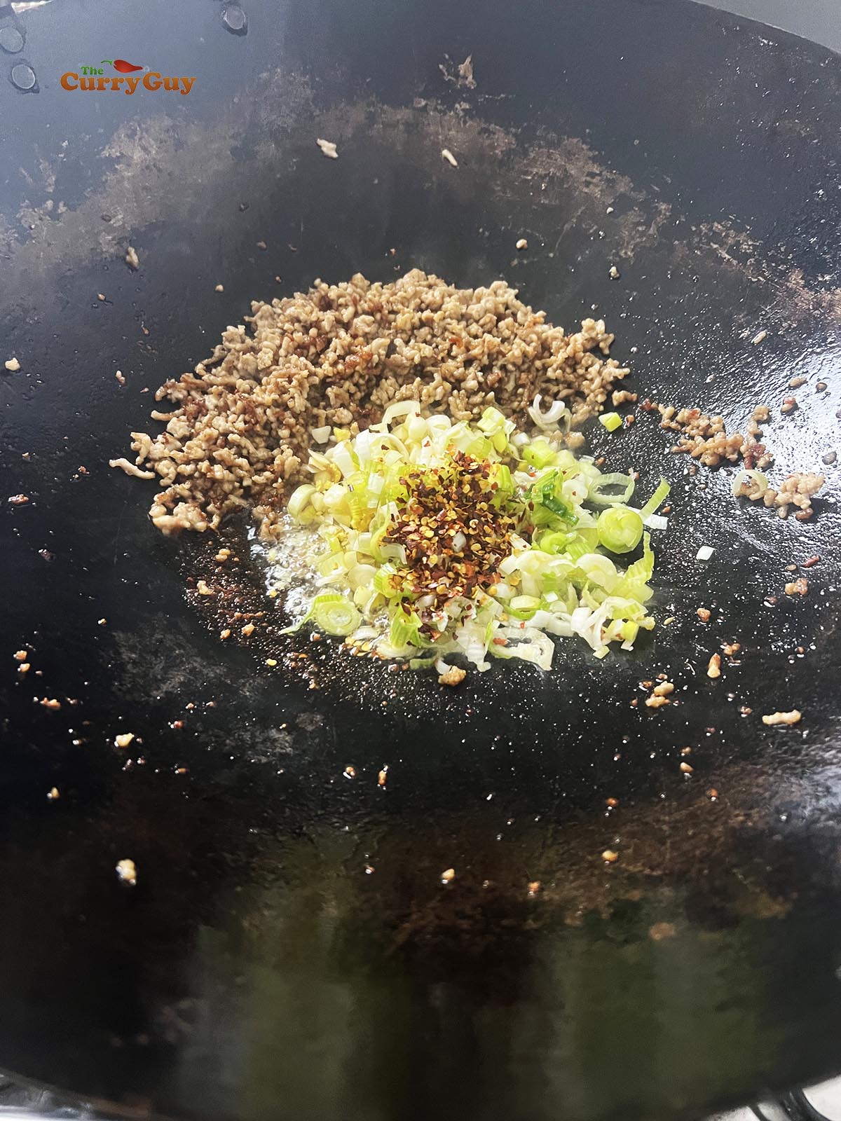 Adding garlic, ginger, spring onions (scallions) and dried chillies to the wok.