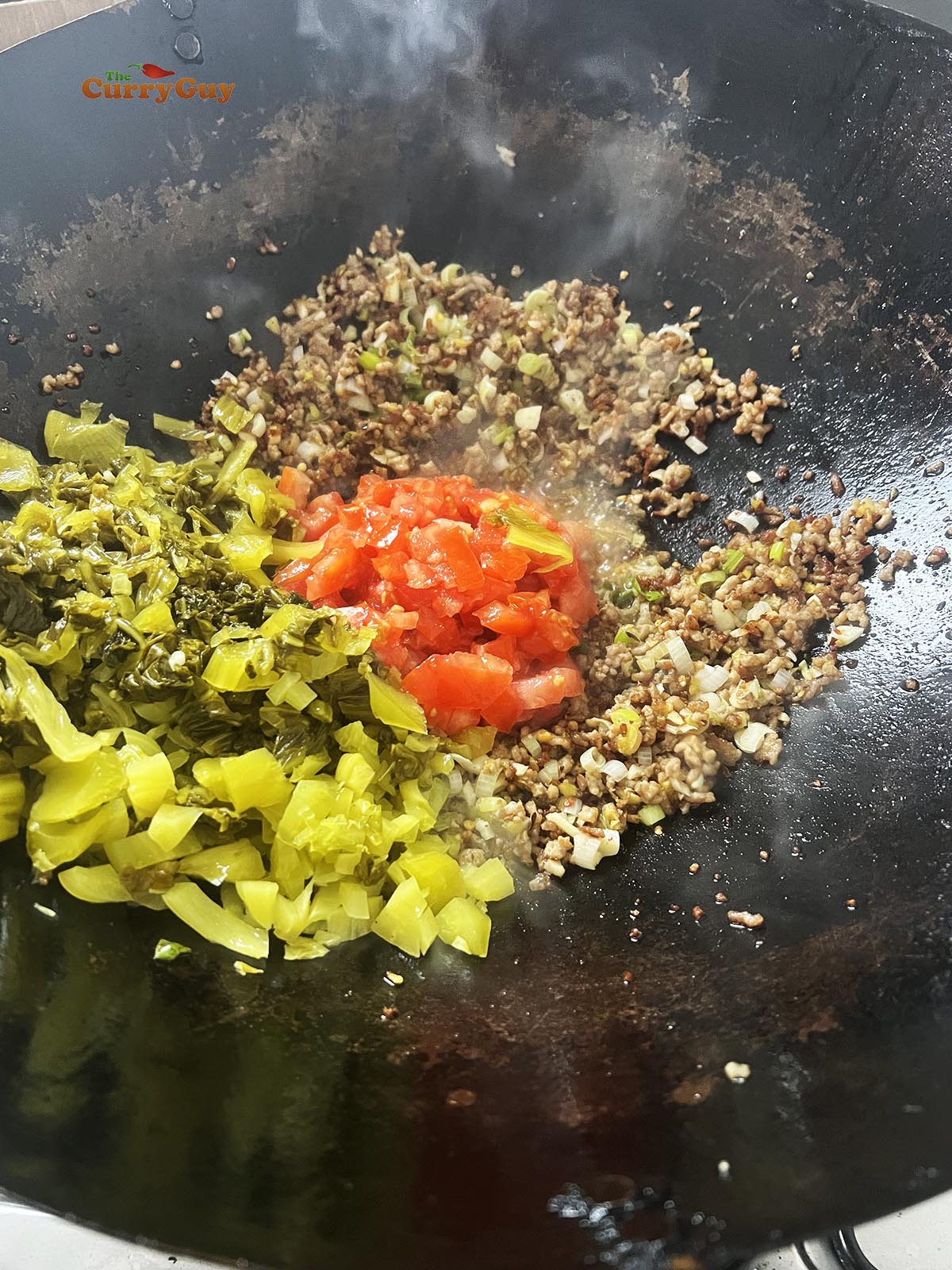 Adding the mustard greens and tomato to the wok.