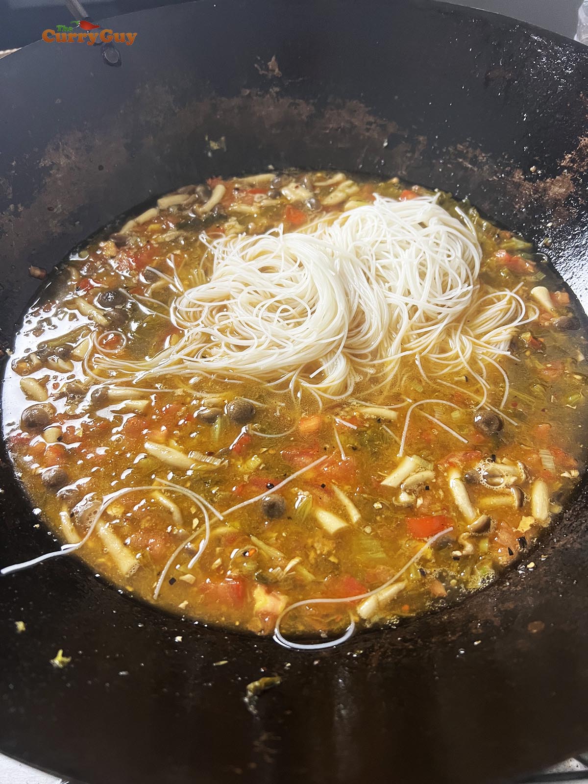 Adding cooked noodles to the soup.