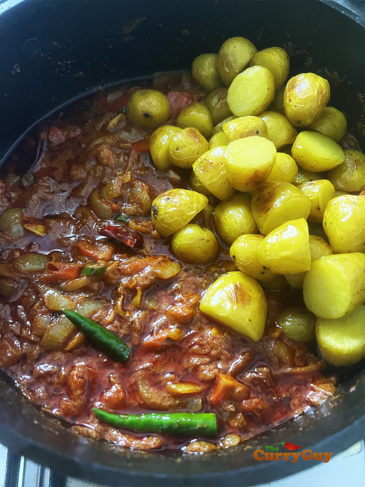 Returning the potatoes to the pan and adding tamarind paste and finger chillies.