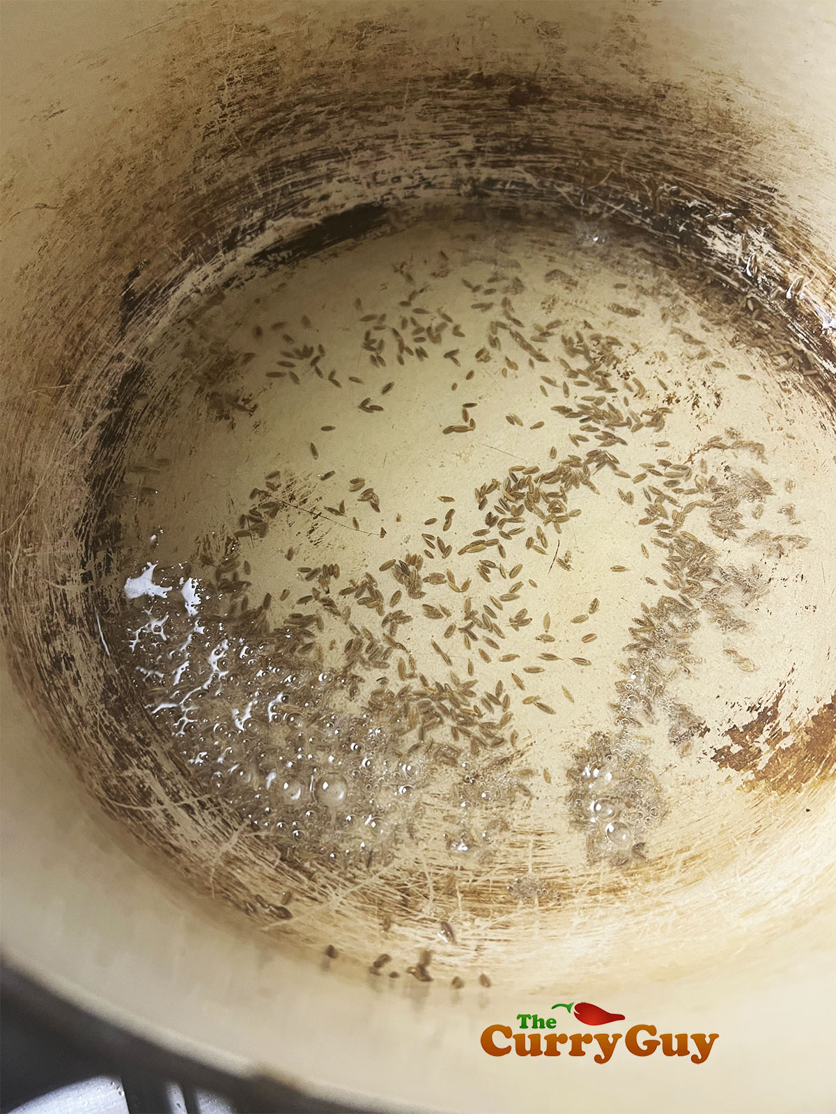Infusing cumin seeds in oil in a pan.