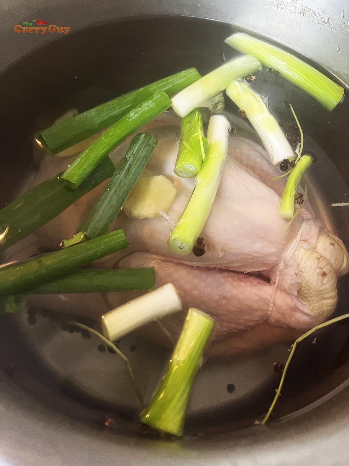 Chicken in a pot with aromatic ingredients, covered with water.