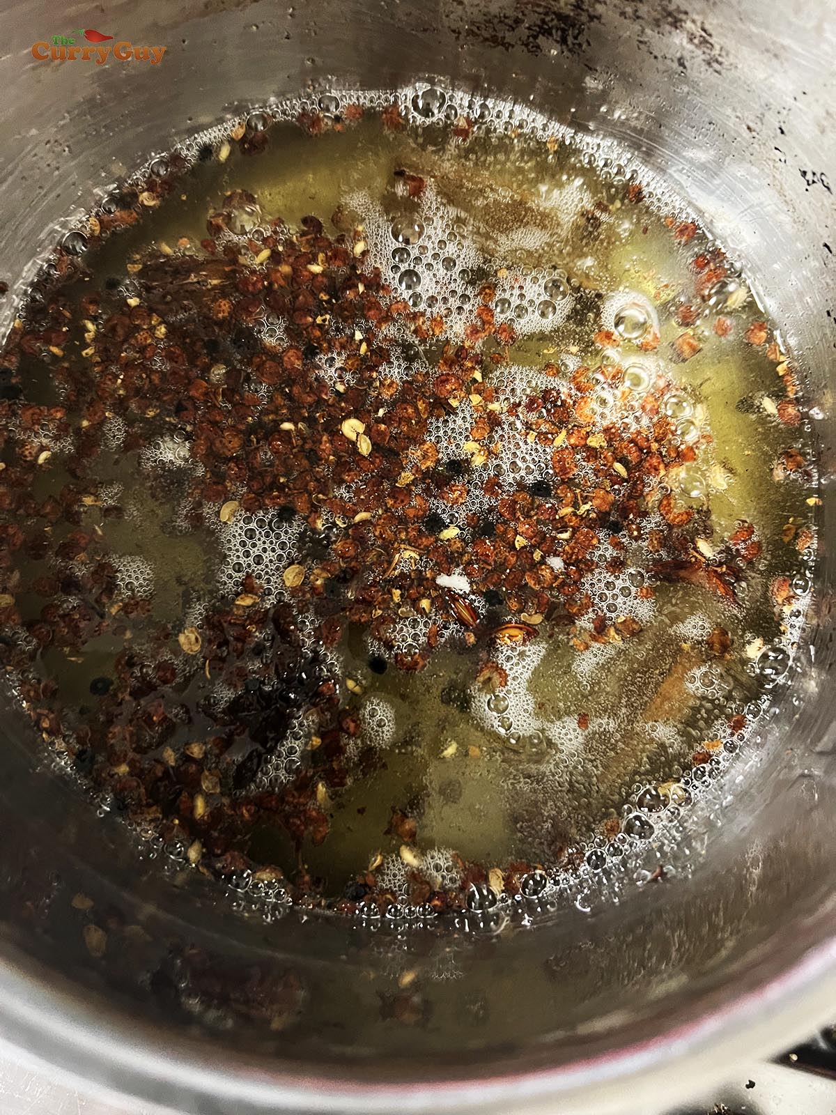 Infusing the whole spices into the oil in a pan.