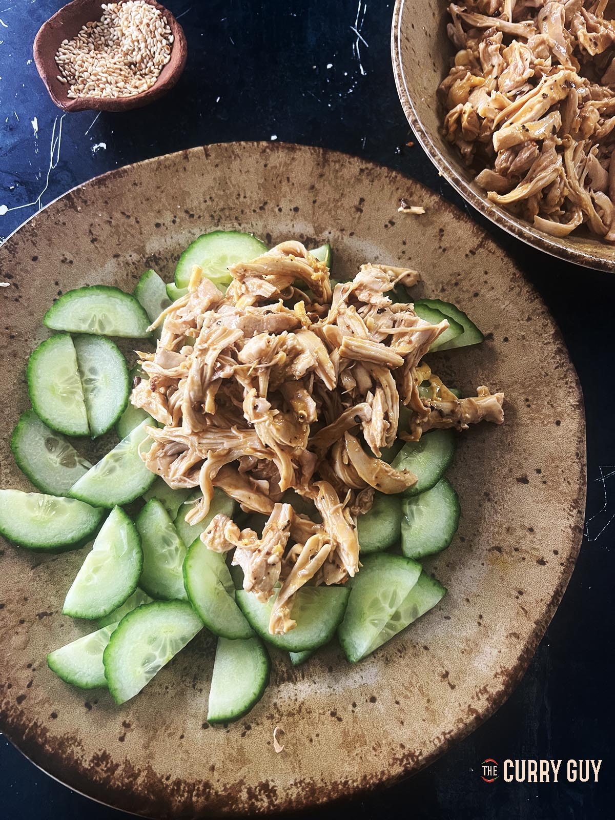 Shredded chicken in the sauce on top of sliced cucumber.