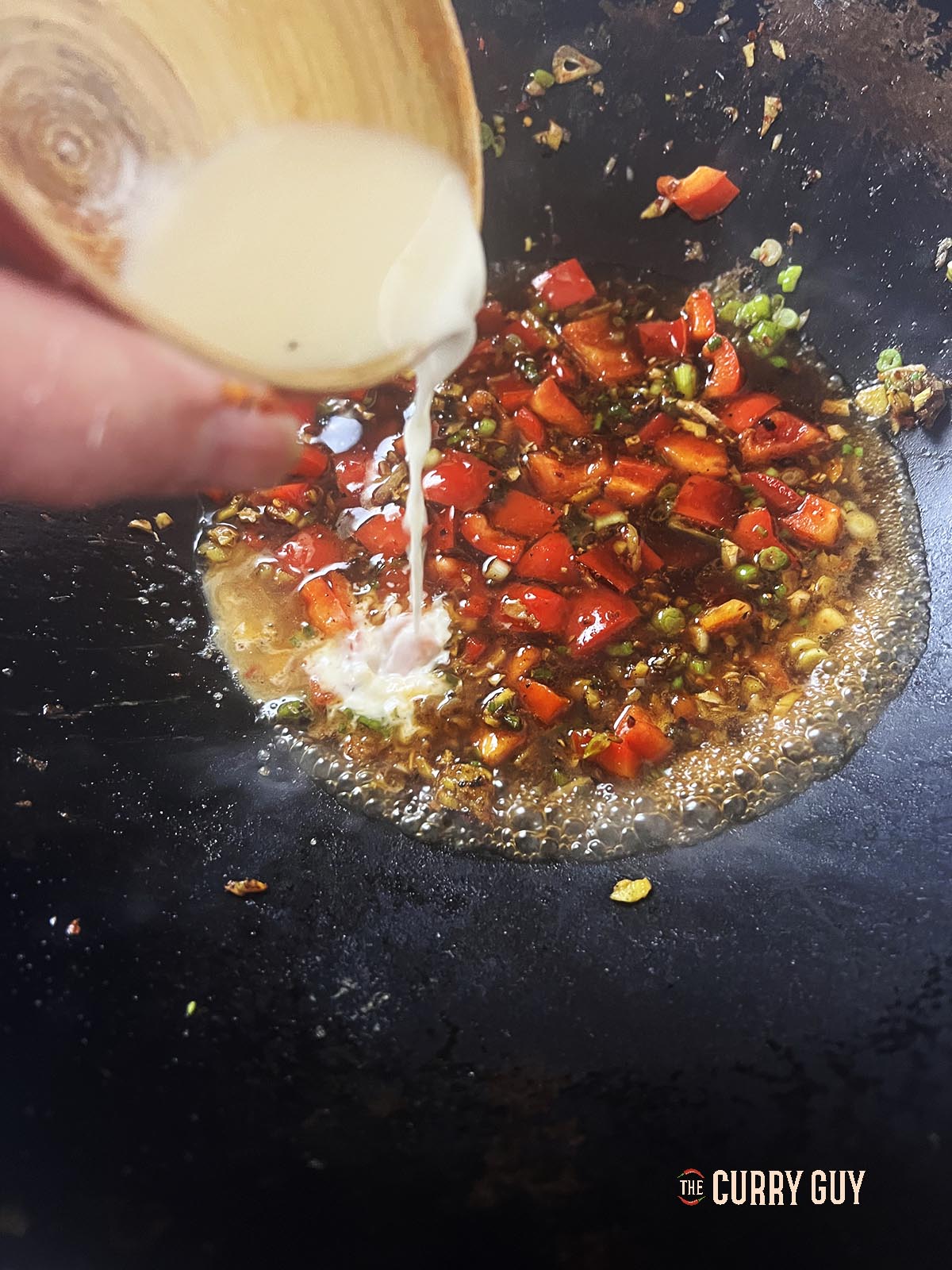 Adding the slurry to thicken the sauce. 