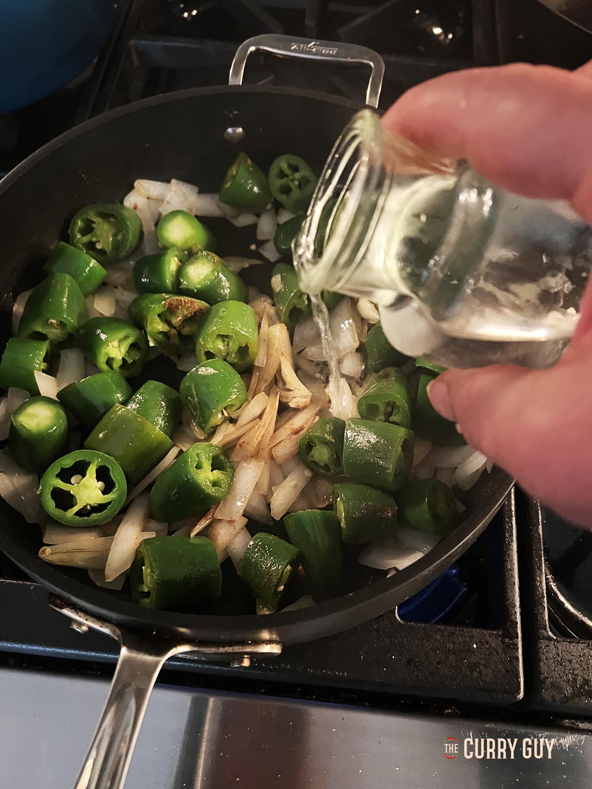 Adding vinegar and water to the chilies, onion and garlic in the pan.