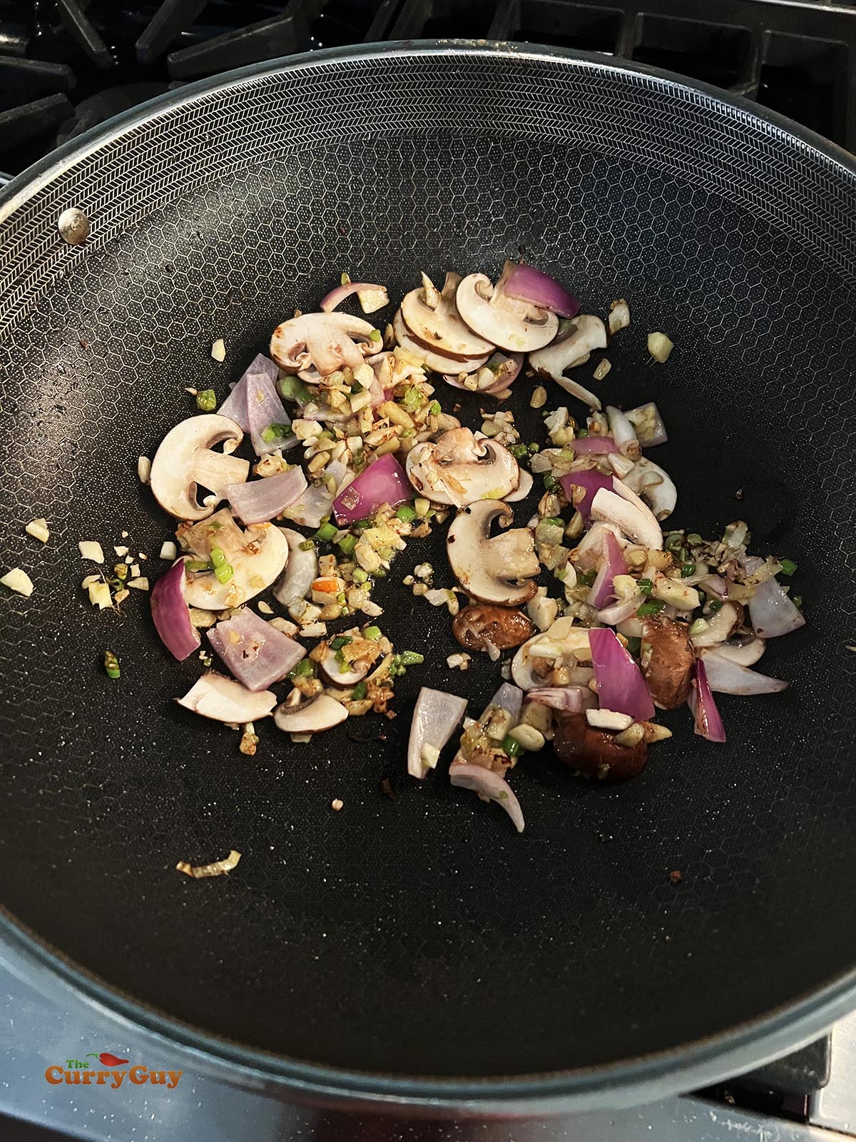 Adding the mushrooms and red onion to the hot wok. 