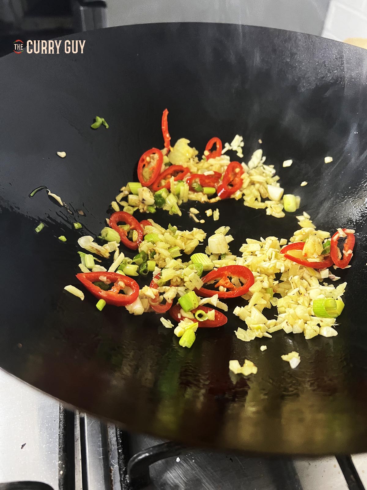 Frying the garlic, ginger, spring onions (scallions) and chilli in sesame oil in a wok.