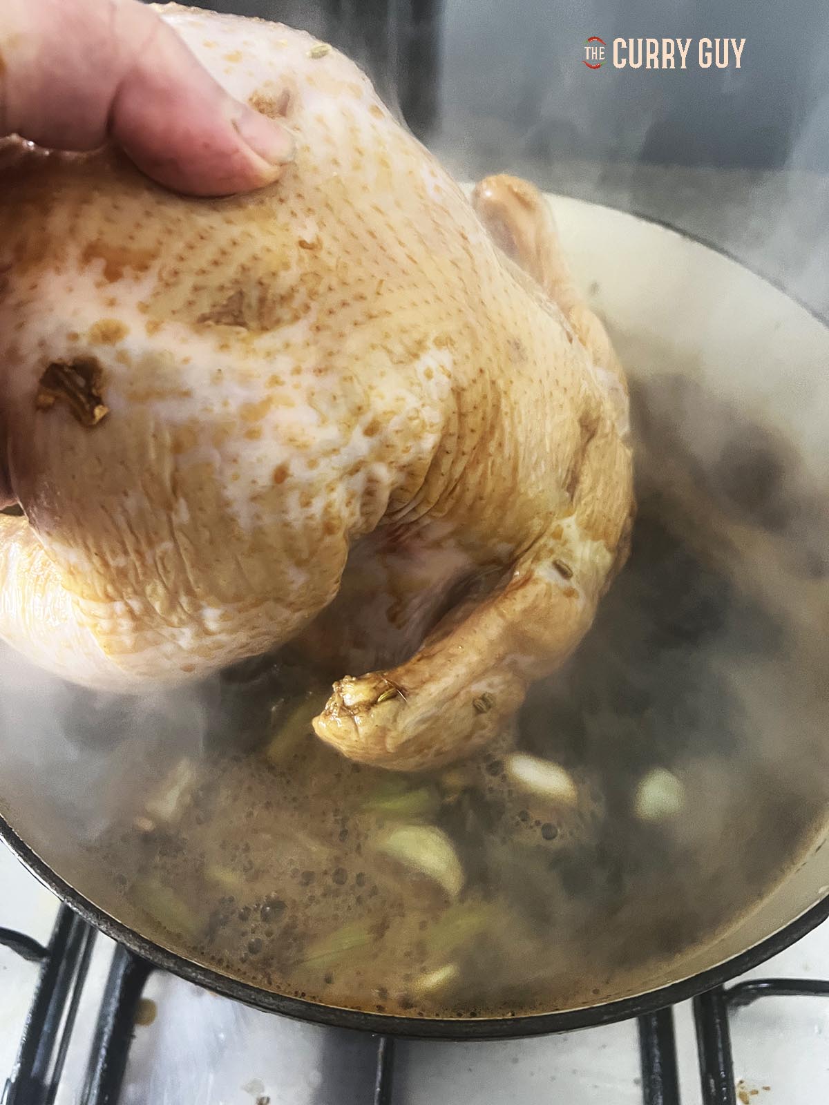 Placing the chicken in the boiling stock in the pot.