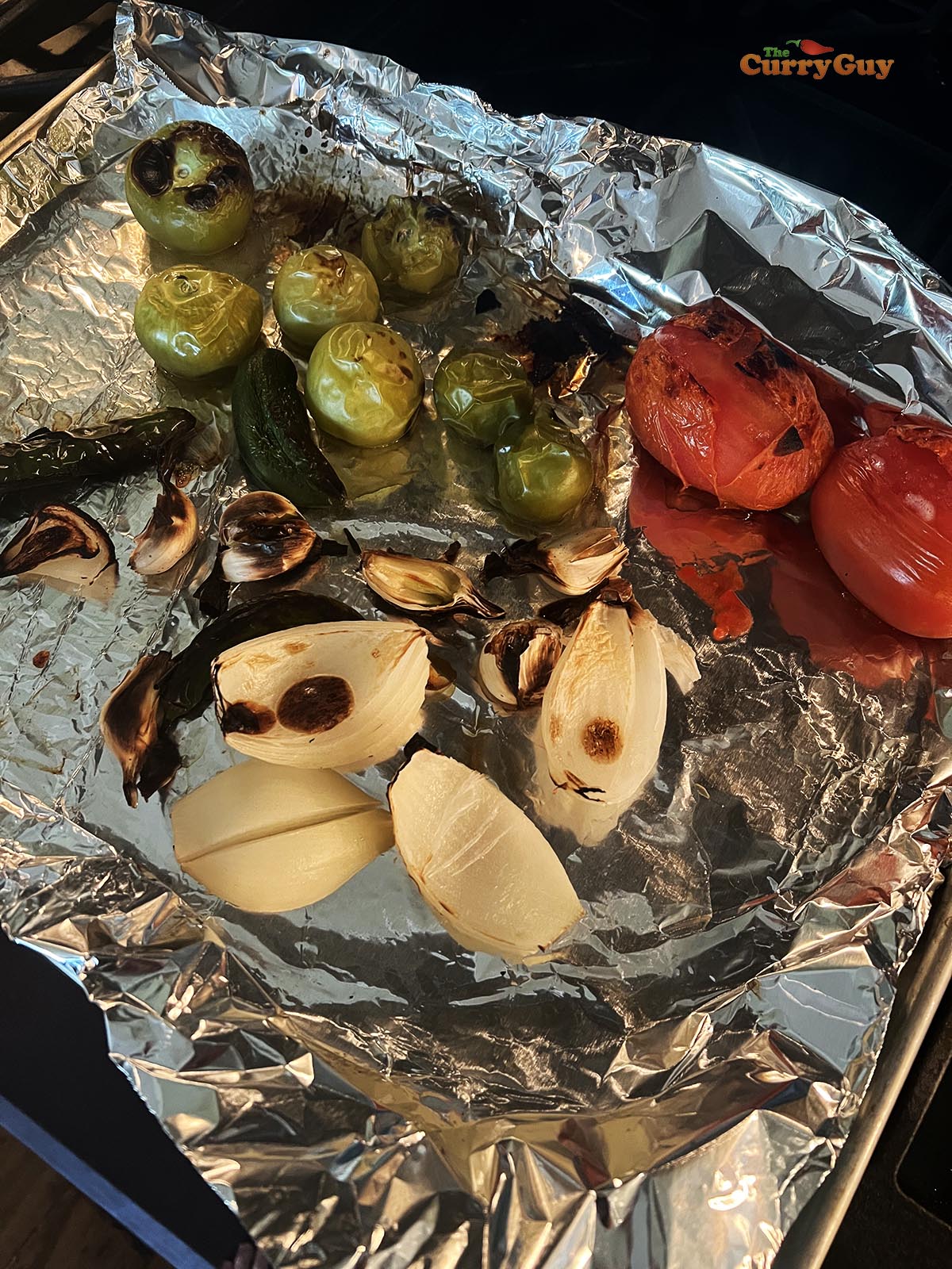 The roasted tomatillos, tomatoes, chillies, garlic and onion on a baking tray.