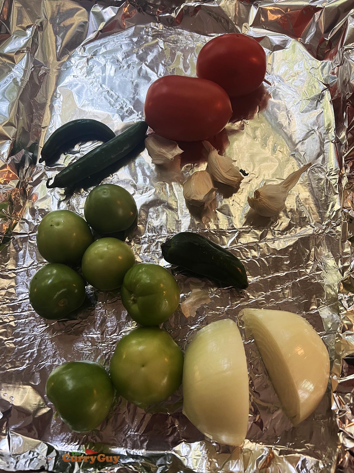 The onions, tomato, garlic, chilies and tomatillos on a foil lined baking tray, ready for roasting.