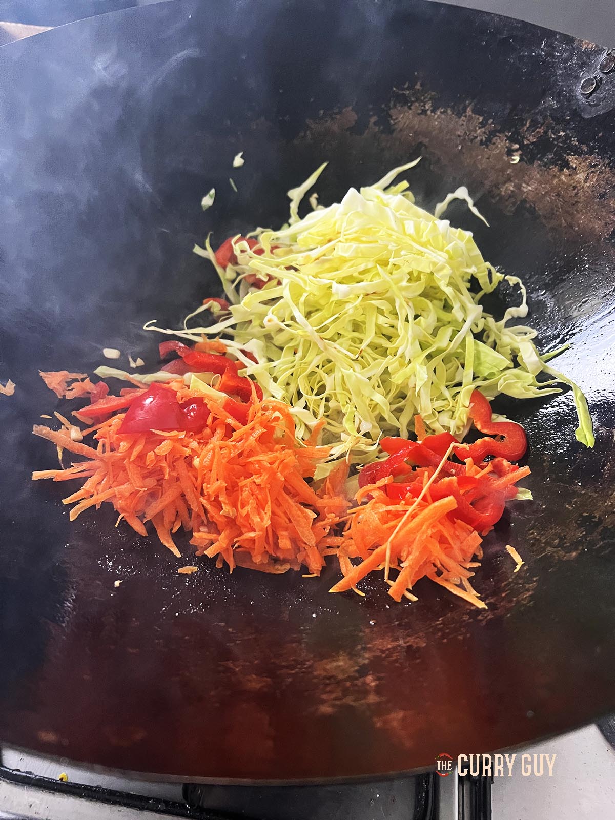Adding the shredded cabbage, grated carrot and sliced bell pepper to the wok.