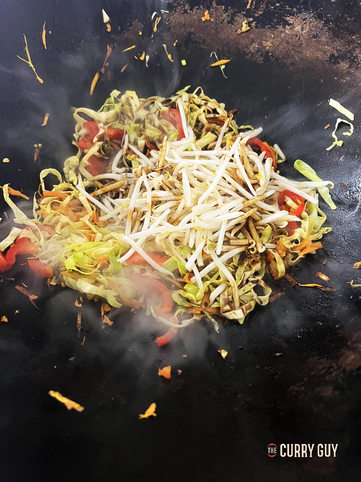 Adding half of the beans sprouts to the other ingredients in the wok.