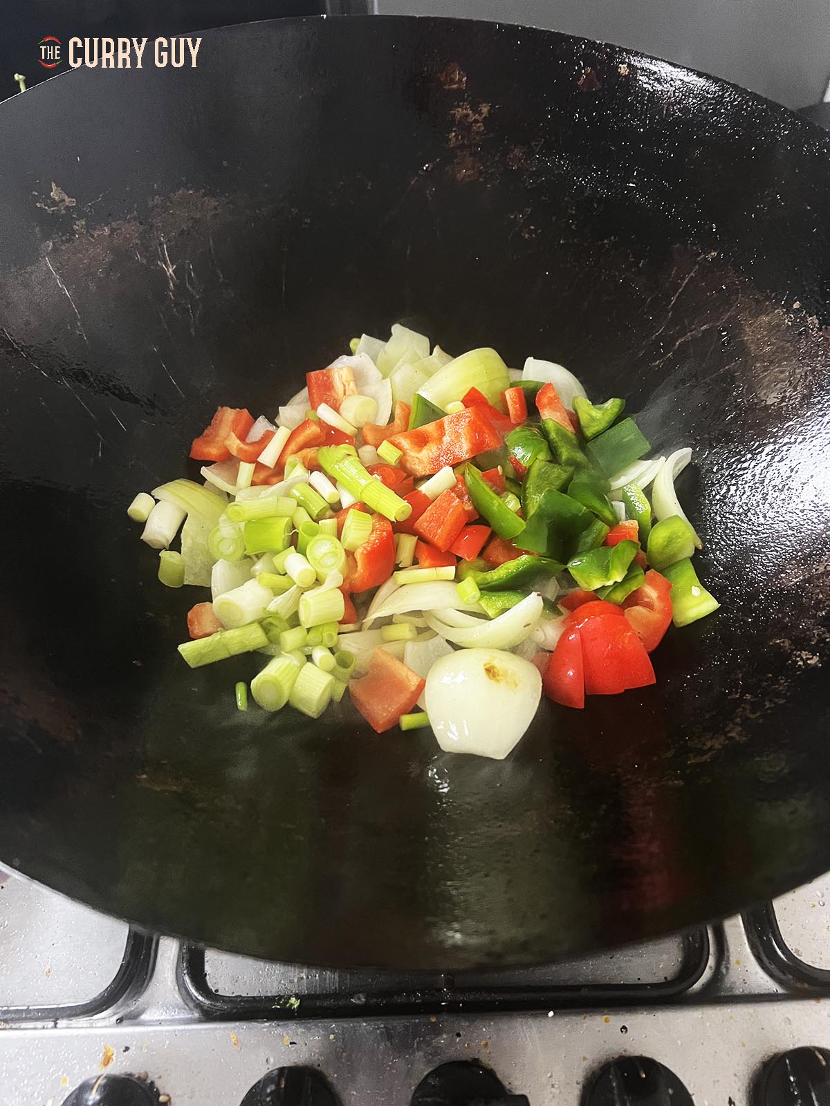 Adding the bell peppers and spring onions (scallions) to the wok.