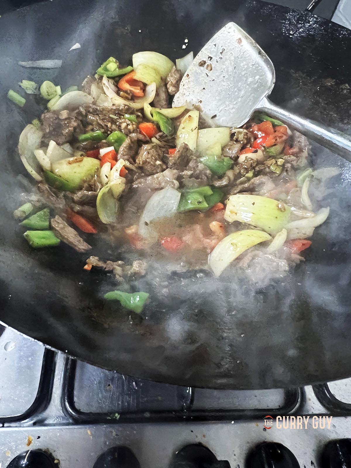 Stirring the ingredients in the wok to combine and adding stock for the sauce.