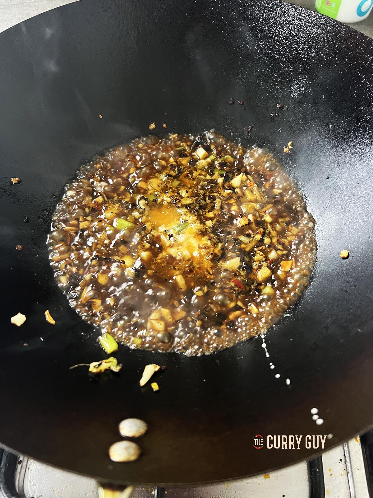 Adding the chicken stock and slurry to the wok.